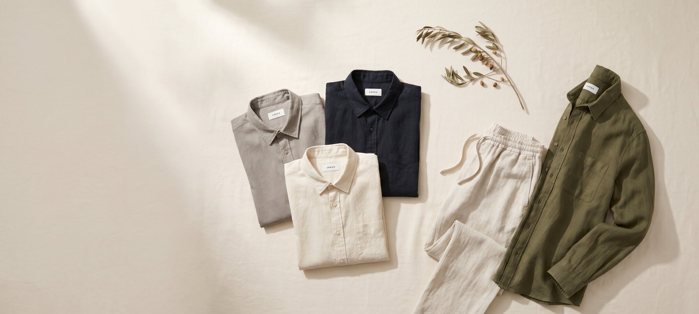 The full ARKEN linen collection — overshirt, shirts, drawstring trousers, on a parchment linen sheet