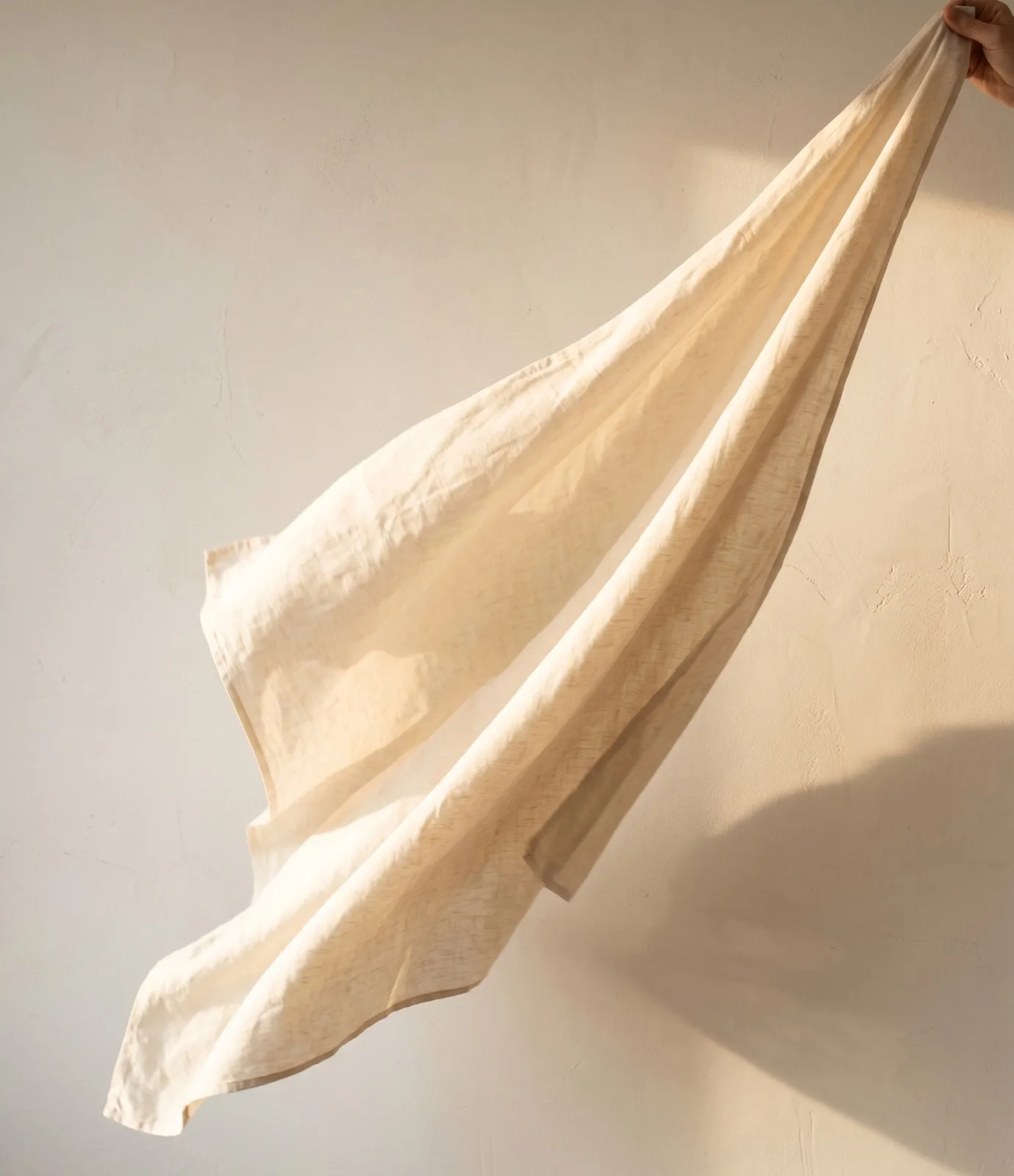 A length of cream linen caught mid-flutter against a limewashed wall
