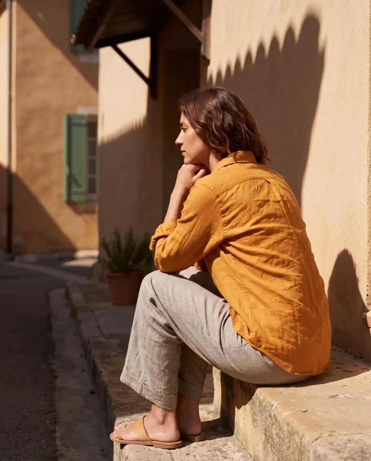 The Cutaway shirt in Saffron — a deep gold-orange linen shirt, Provençal stone wall behind.